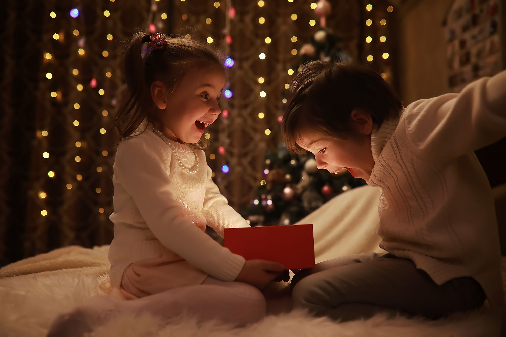 Family on Christmas eve at fireplace. Kids opening Xmas presents Family on Christmas eve at fireplace. Kids opening Xmas presents. Children under Christmas tree with gift boxes. Decorated living room with traditional fire place. Cozy warm winter evening home.