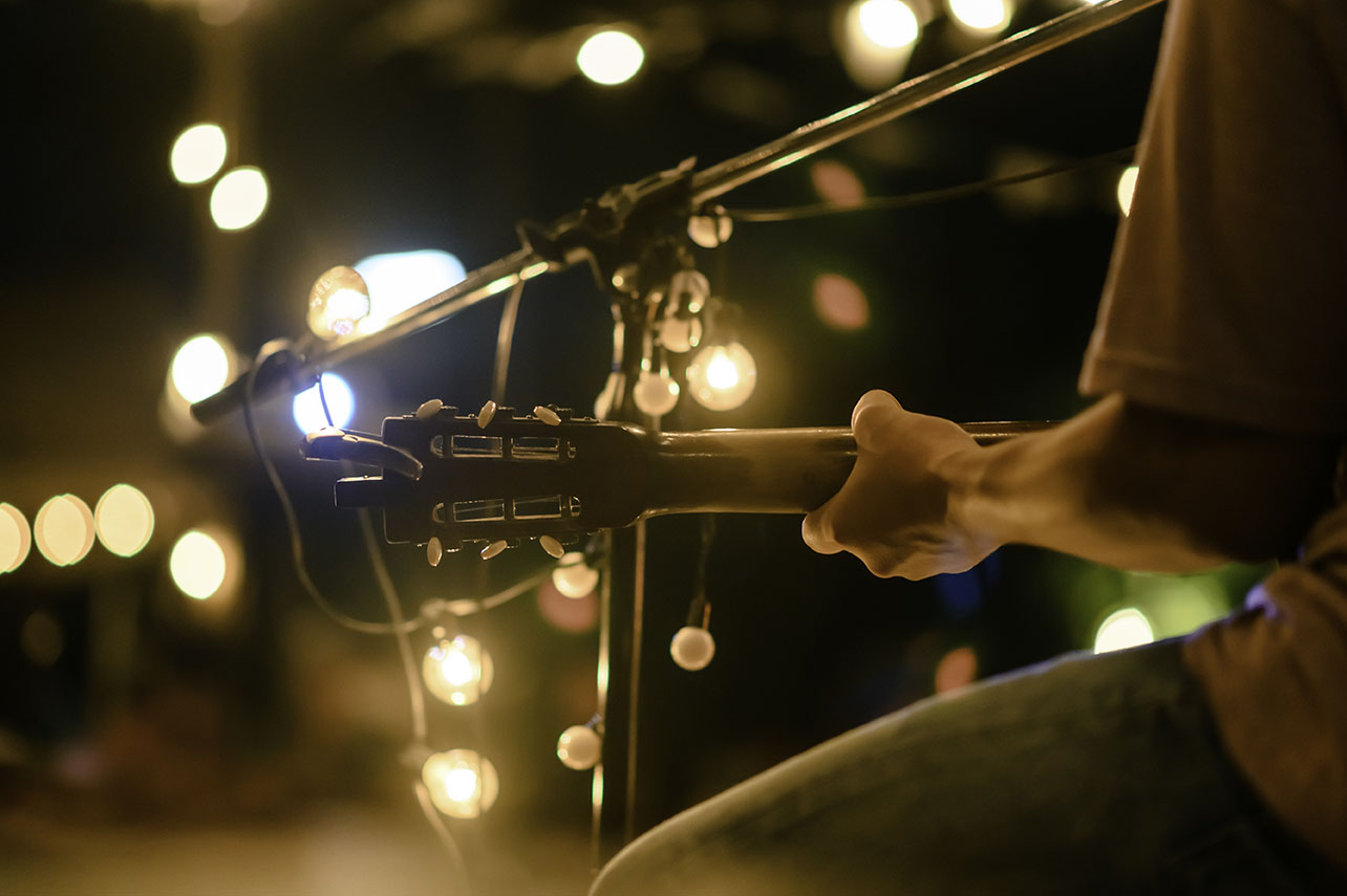 Rear view of the man sitting play acoustic guitar on the outdoor concert with a microphone stand in the front, musical concept.