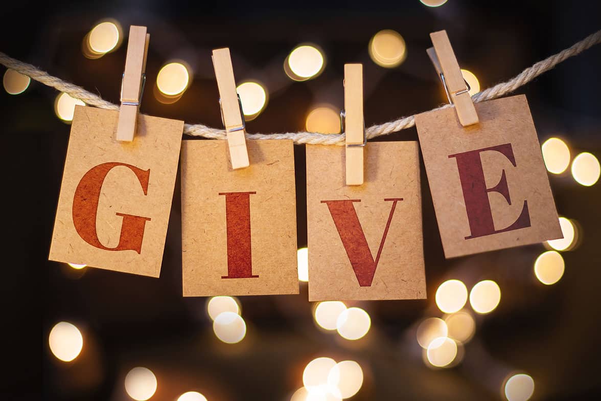 The word GIVE spelled out on clothespin clipped cards in front of glowing lights.