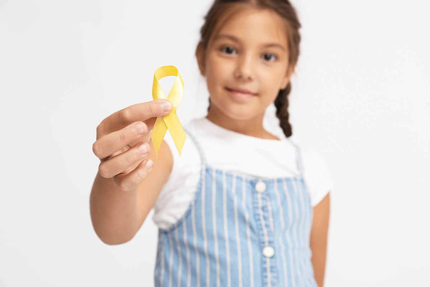 Little girl with golden ribbon on light background. Childhood cancer awareness concept